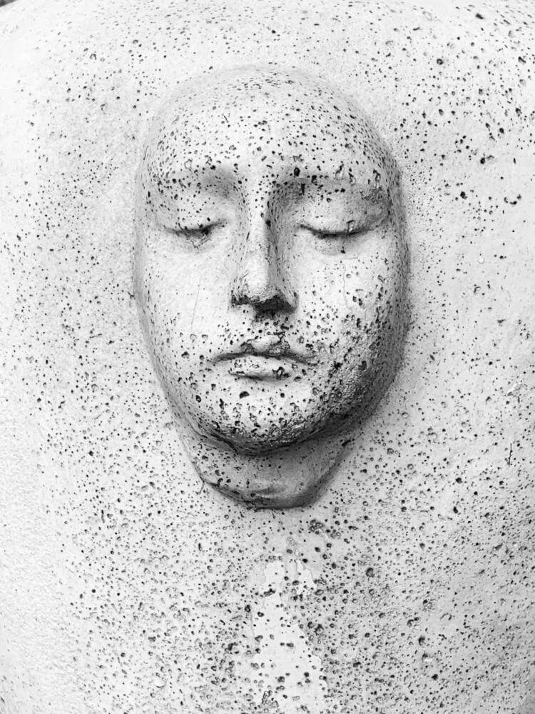 Sculpture of a face looking down in an oval shape and pitted exterior